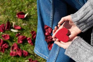 Hands holding a red heart symbol with rose petals scattered, representing healing and self-awareness in relationships.