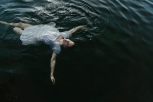Person floating in dark water representing feeling overwhelmed and seeking help from an addiction therapist