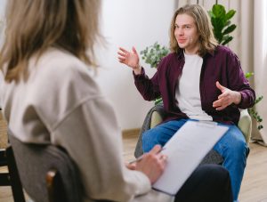 A man sits in a therapy session, speaking with a clinician and smiling while engaging in CBT therapy on Long Island