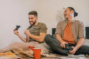 Two men play video games together, smiling and relaxed, after trauma therapy on Long Island
