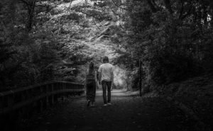 A couple walking through a serene forest park in grayscale, creating a peaceful atmosphere.